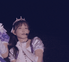 a woman wearing a tiara and gloves is speaking into a microphone