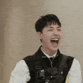 a young man wearing a black vest and tie is laughing with his mouth wide open