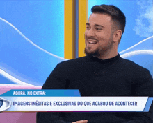a man with a beard is smiling while sitting in front of a sign that says agora no extra