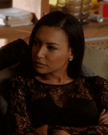 a woman wearing a black lace top sits on a couch