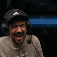 a man wearing headphones and a hat laughs with his mouth open