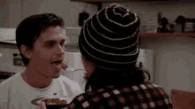a man wearing a striped hat is feeding another man a piece of cake