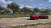a red car is driving down a road with trees in the background