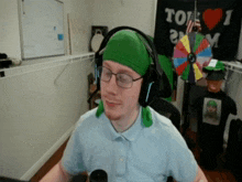a man wearing headphones and a green headband stands in front of a sign that says " i love tom "