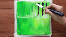 a person is using a knife to spread green paint on a piece of paper .