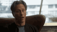 a man is sitting in a chair with his mouth open and a surprised look on his face .