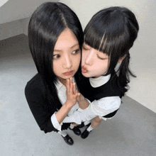 two girls are standing next to each other and one of them is kissing the other on the cheek