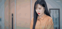 a woman with long black hair and red lips is wearing a yellow shirt .