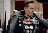 a man in a military uniform is standing in a room with medals on his chest .