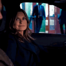 a woman is sitting in the back seat of a car with a man in a suit behind her