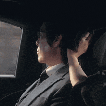 a man in a suit sits in the back seat of a car with his hand on his head