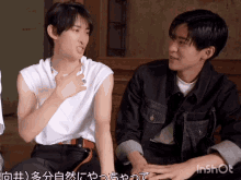 two young men are sitting next to each other and one has his hand on the chest of the other