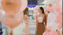 two women are standing next to each other in front of balloons .
