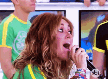 a woman singing into a microphone with a sbt logo in the corner