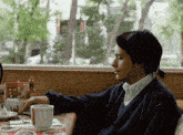 a man sits at a table with a cup of coffee and a cigarette in his mouth