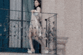 a woman in a white dress is standing on a balcony holding onto a railing .
