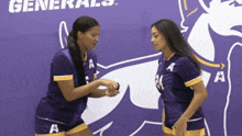two girls shake hands in front of a purple generals sign
