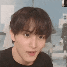 a close up of a young man making a funny face while wearing a black t-shirt .