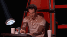 a man is sitting in a red chair with two cups of coffee