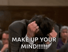 a man in a suit is holding his head in his hands and says `` make up your mind !!! ''