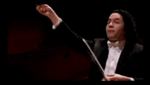 a man in a tuxedo is holding a baton and giving a thumbs up sign