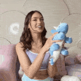 a woman in a purple top is holding a blue stuffed unicorn .
