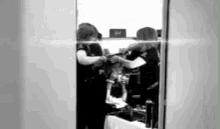 a black and white photo of a woman getting her hair done in front of a mirror