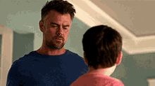 a man and a boy are standing next to each other in a room . the boy is wearing a pink shirt .