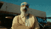 a man wearing a ski mask is standing in front of a plane with the word trust on the side