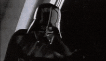 a black and white photo of darth vader wearing a helmet from star wars .