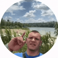 a man in a blue shirt is standing in front of a lake and pointing at it .