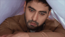 a man with a beard is laying under a blanket and looking down