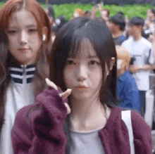 a girl in a purple jacket is making a funny face while standing next to another girl in a crowd .