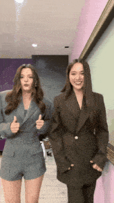 two women in suits are standing next to each other and giving thumbs up
