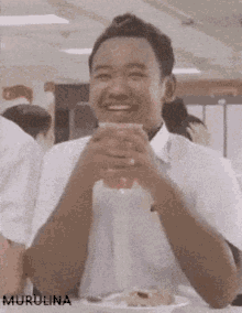 a man in a white shirt is sitting at a table with a plate of food and a drink in his hand ..
