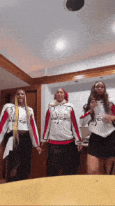 three women are standing in a room wearing adidas shirts