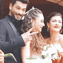 a man in a tuxedo is giving a peace sign to a bride and groom .
