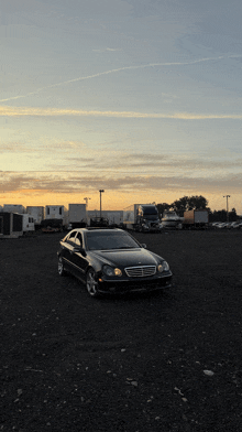 a black mercedes is parked in a gravel lot