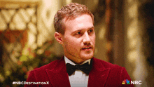 a man in a red tuxedo and bow tie with the nbc destination x logo behind him