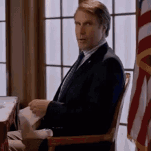 a man in a suit and tie is sitting in a chair in front of a window .