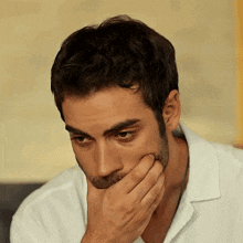 a man with a beard and a white shirt covering his mouth with his hand