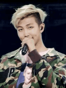 a young man wearing a camouflage jacket is singing into a microphone .