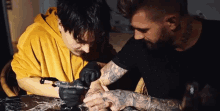 a man is tattooing another man 's arm with a machine .