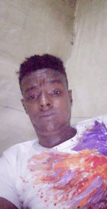 a man in a white t-shirt with a painting on it is taking a selfie .