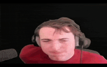 a young man wearing headphones and a red shirt is looking at the camera .