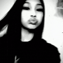 a black and white photo of a girl blowing a kiss with her mouth open .