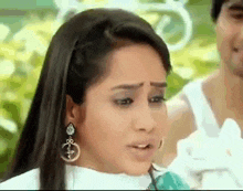 a woman wearing earrings is making a funny face while a man looks on .