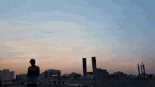 a man stands on a rooftop looking at a sunset over a city