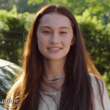a woman with long hair is smiling and wearing a white shirt and a necklace .