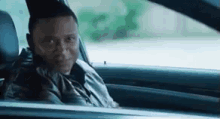 a man is sitting in the driver 's seat of a car and looking out the window .